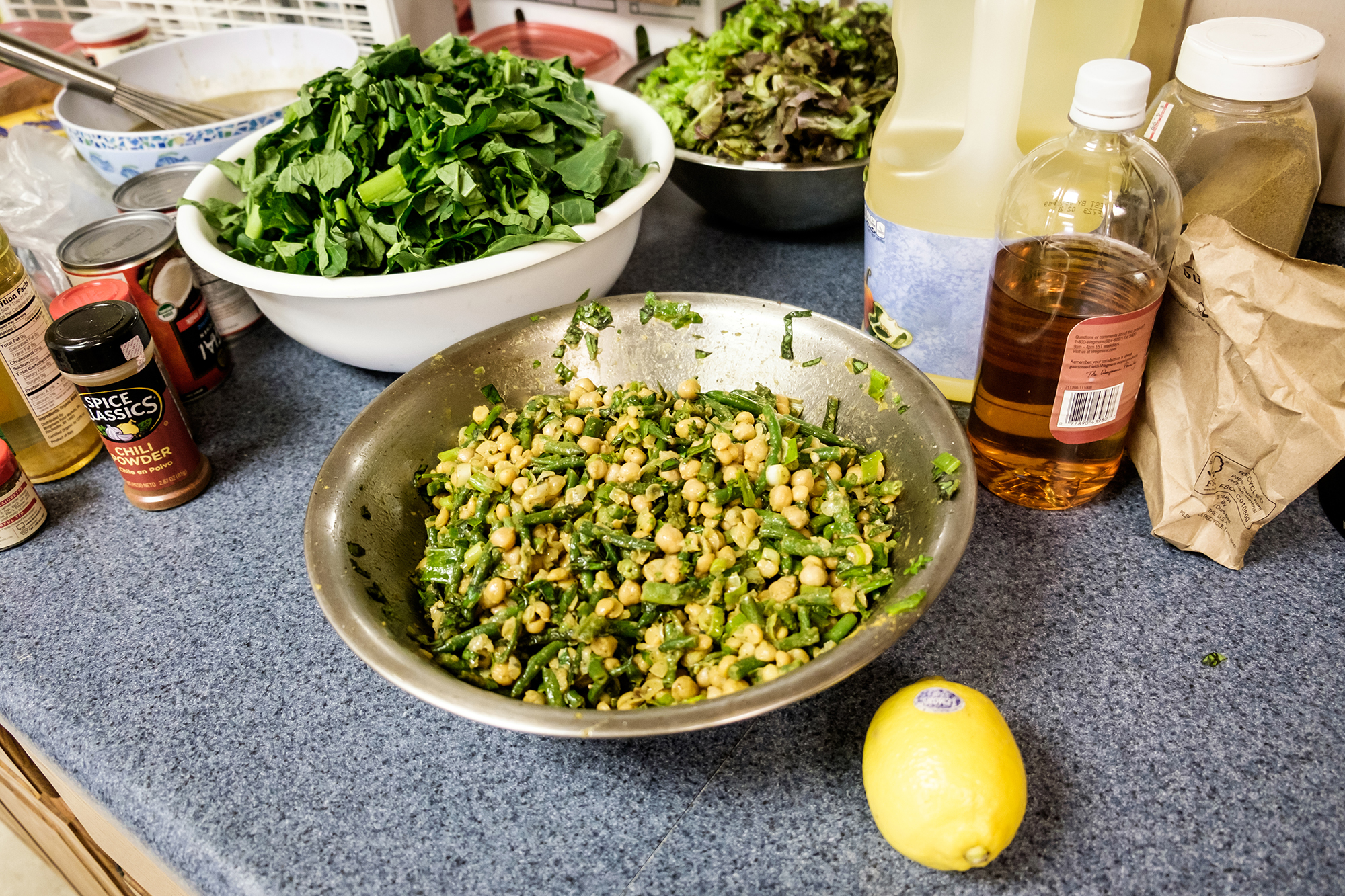 several bowls with mixed greens in the kitchen with cooking materials surrounding the bowls