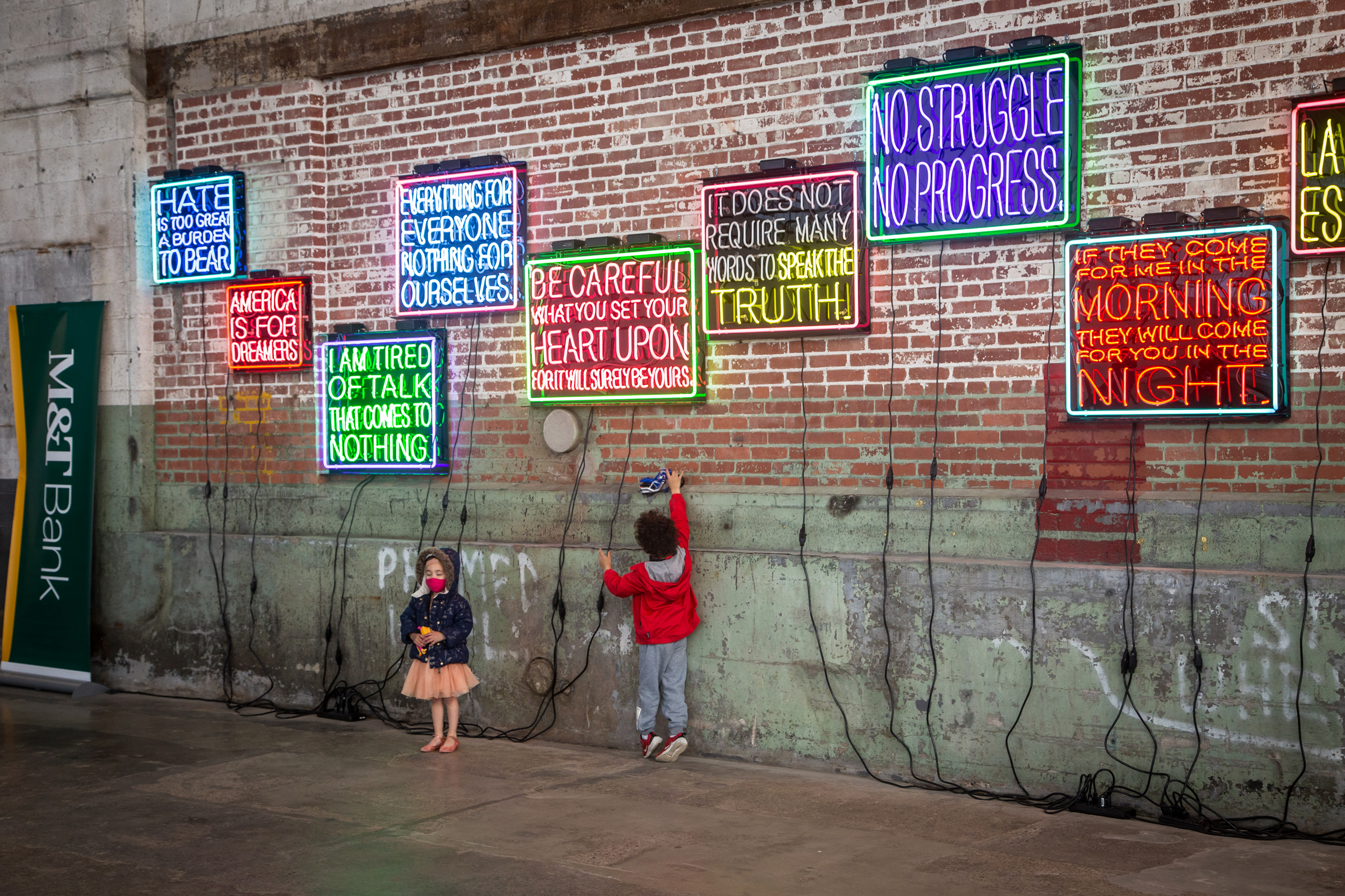 two kids standing in front of neon signs hanging on the side of a brick building