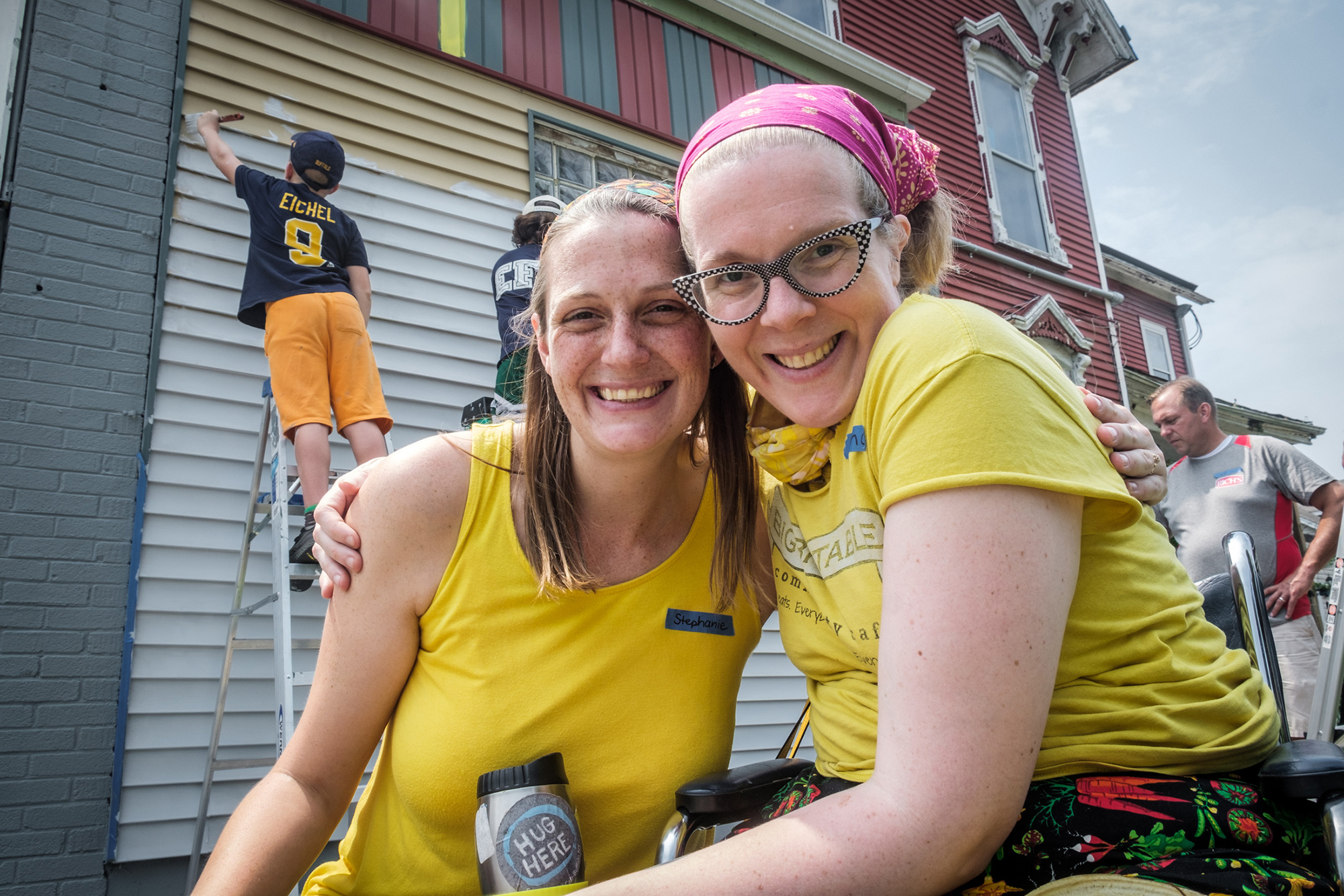 two women smiling for photo in front of building being painted by volunteers