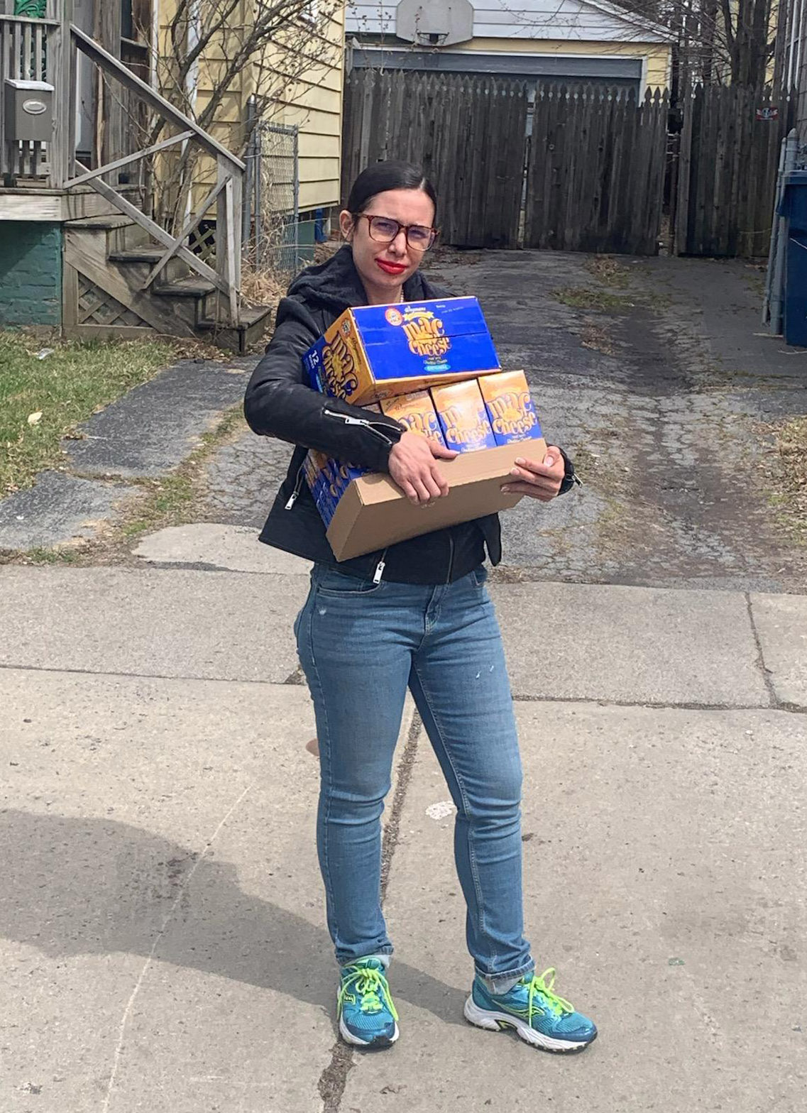 woman standing on the sidewalk holding several boxes of macaroni and cheese