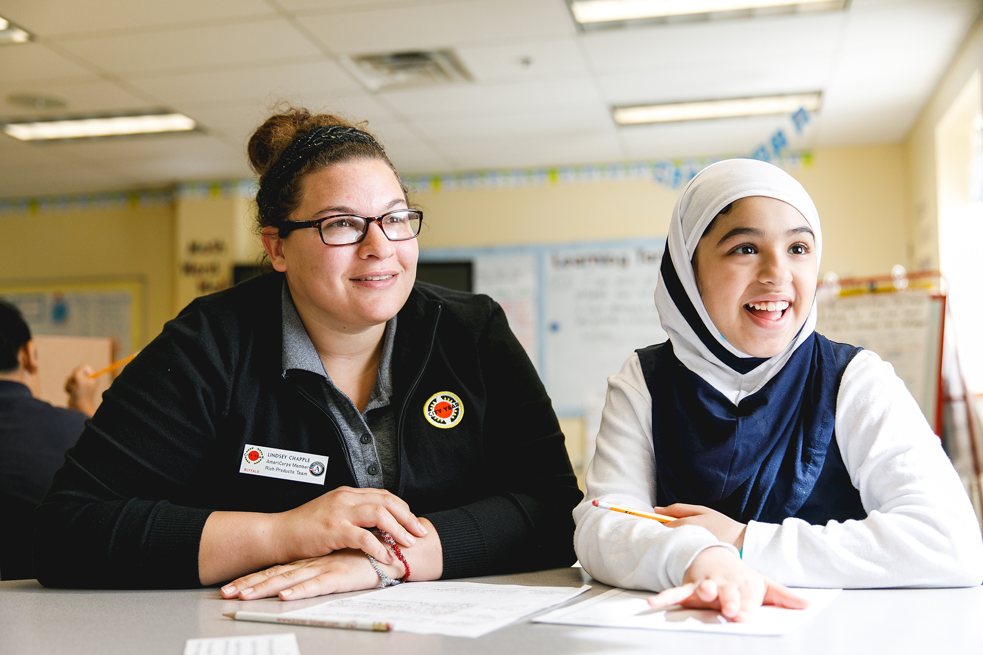 a female americorps volunteer and younger girl actively listening and looking