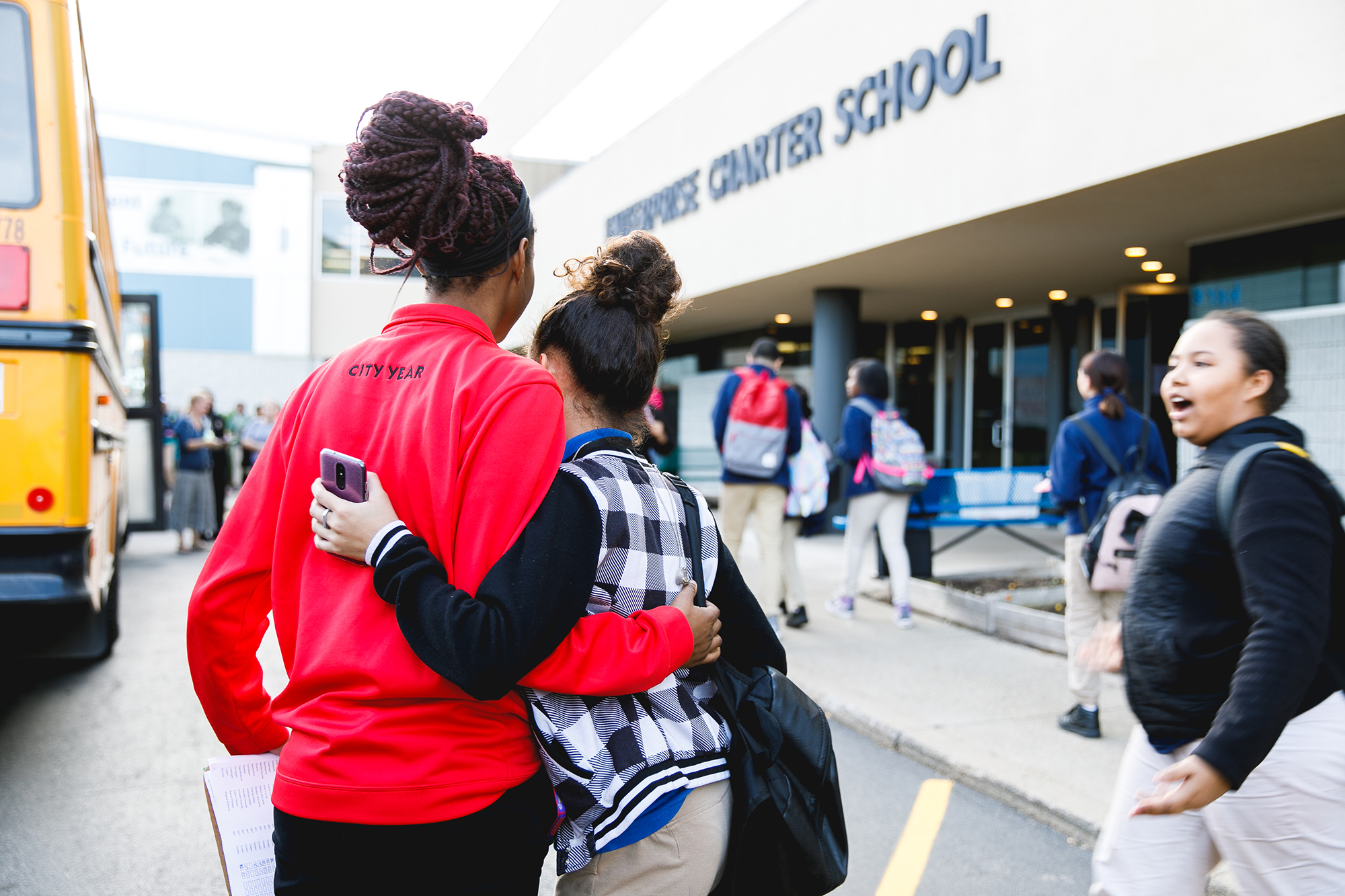 americorps volunteer and student hugging in front of enterprise charter school