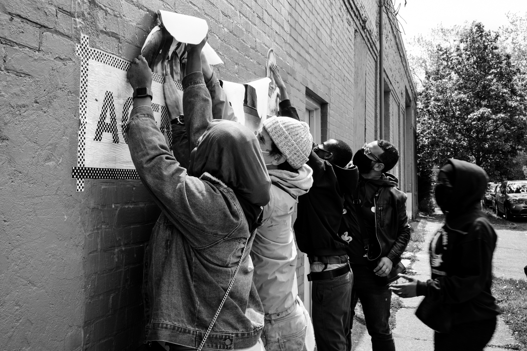 black and white photo of people hanging the agent of change sign on the side of a brick building