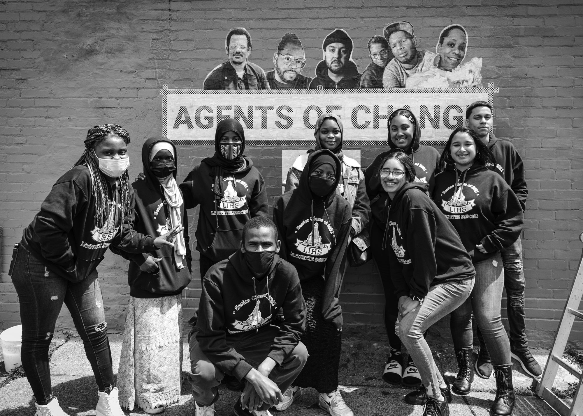 black and white photo of a group of people standing in front of the agents of change sign on the side of a brick building