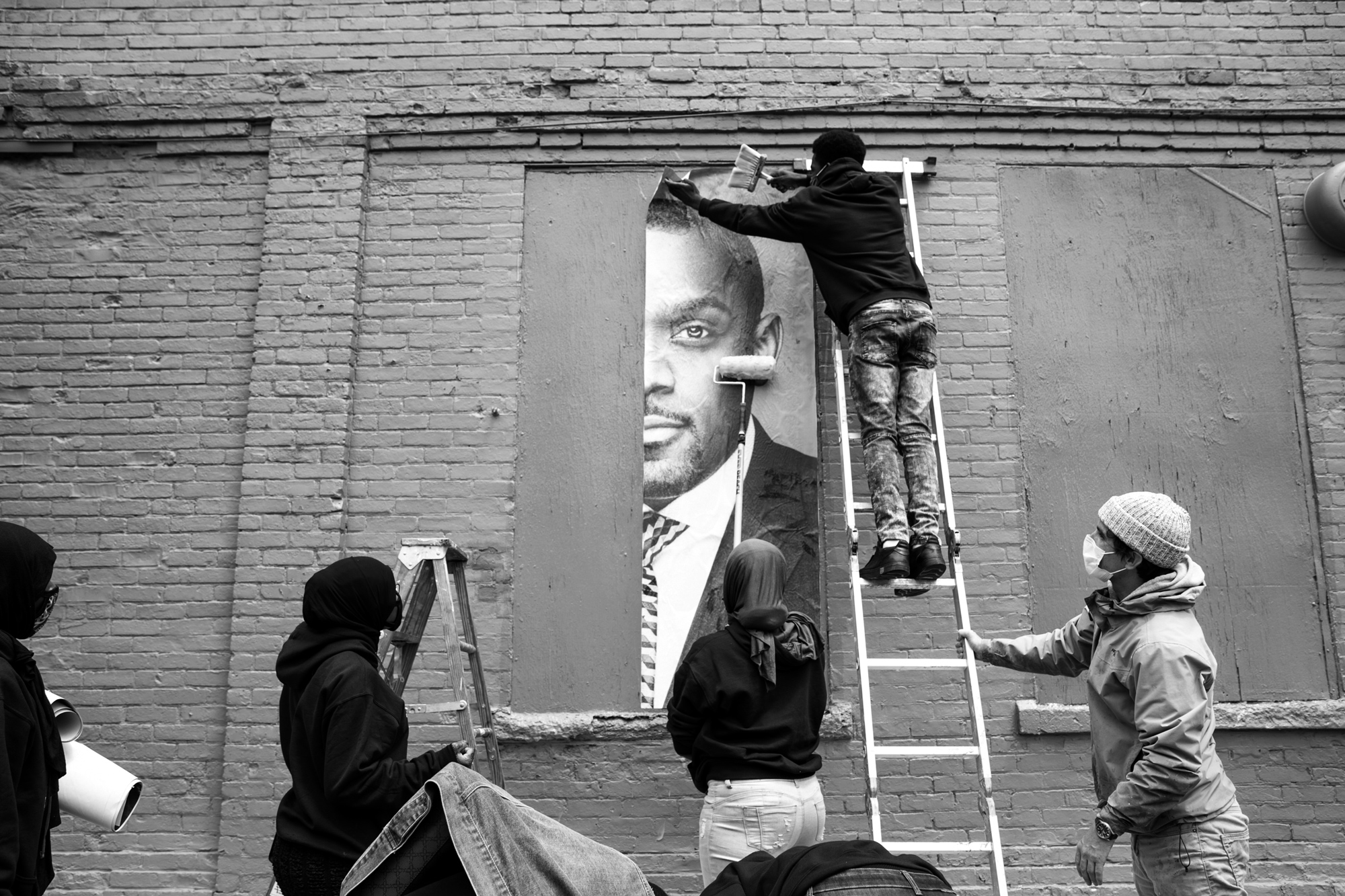 black and white photo of people hanging a person's portrait on the side of a brick building