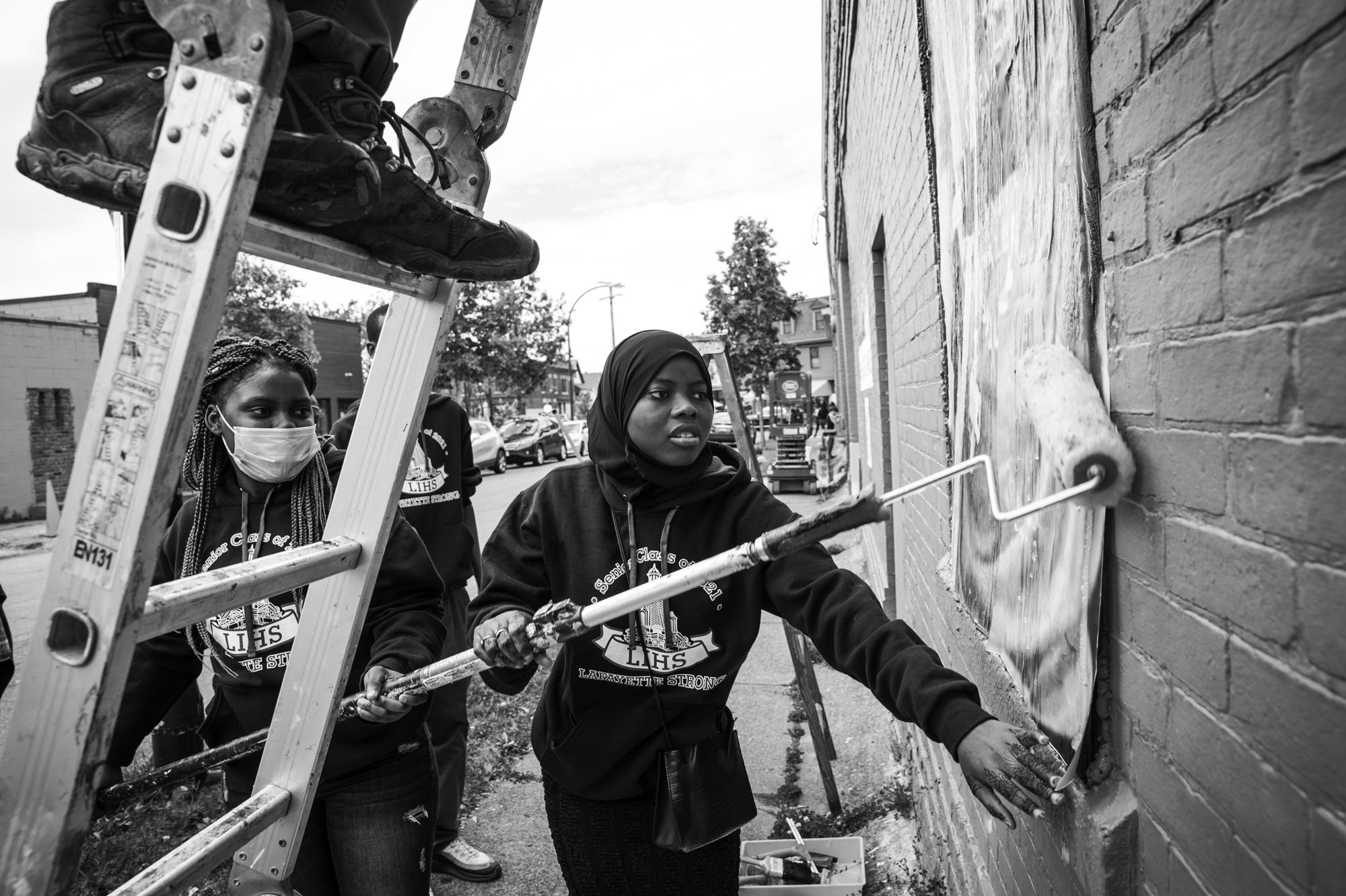 black and white photo of a group of students hanging canvas on the side of a brick building