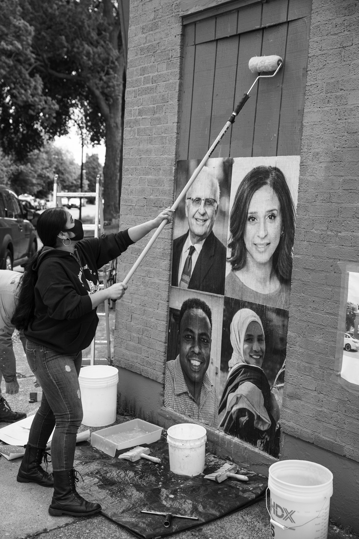 woman using a paint roller to hang people's portraits on the side of a building