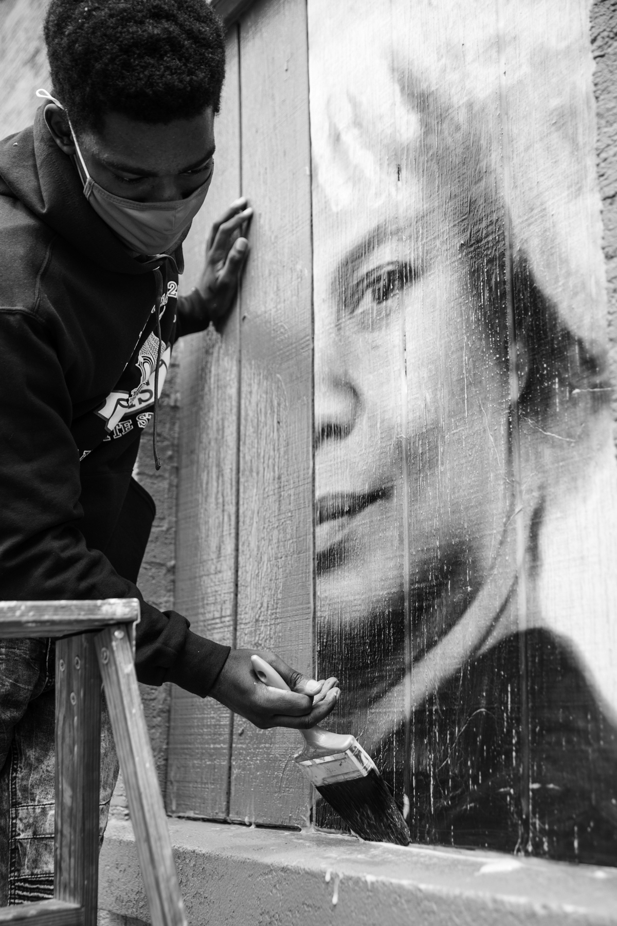 black and white photo of man painting a person's portrait onto the side of wood paneling