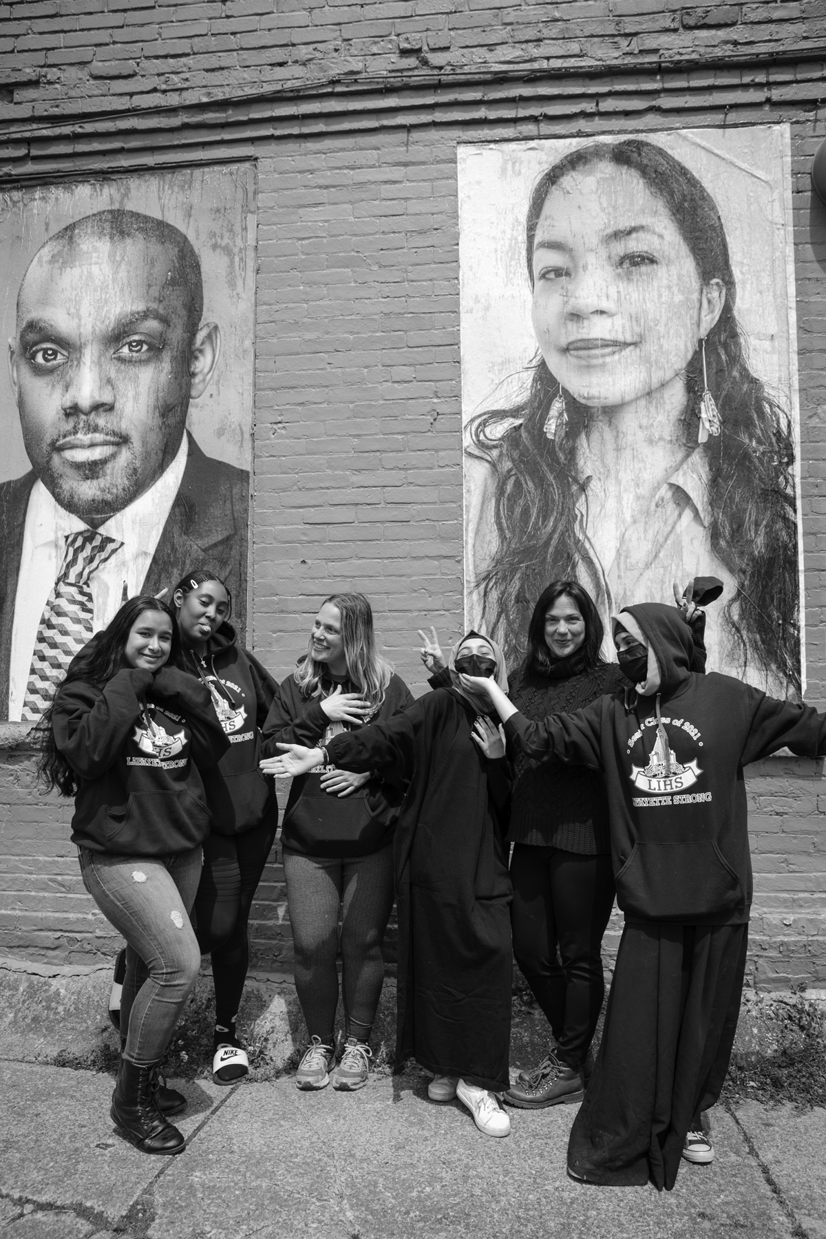 black and white photo of women posing in front of two portraits on the side of a brick building